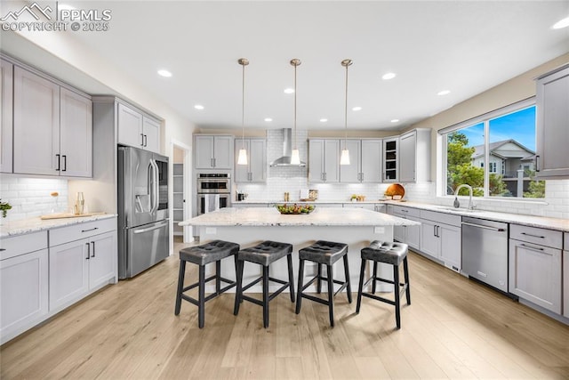 kitchen with wall chimney exhaust hood, light wood-style flooring, a breakfast bar, stainless steel appliances, and a sink