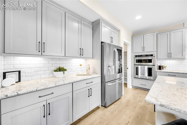 kitchen with stainless steel appliances, light wood-type flooring, light stone countertops, and tasteful backsplash