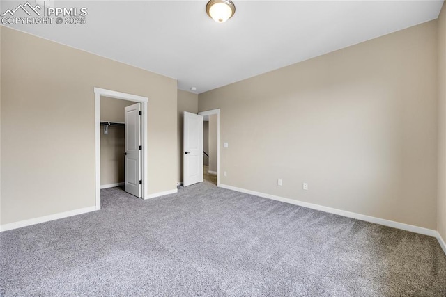 unfurnished bedroom featuring a closet, carpet, a walk in closet, and baseboards