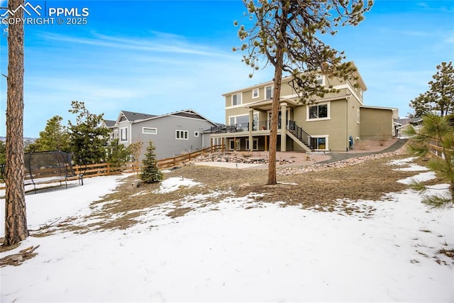 snow covered house featuring stairs, a trampoline, and fence