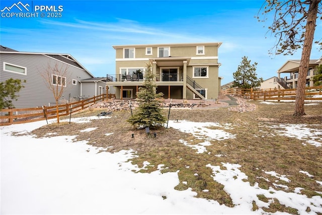 snow covered back of property with stairway, fence, a balcony, and stucco siding