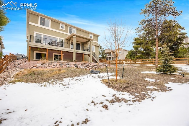 snow covered rear of property featuring stairway, fence, and stucco siding