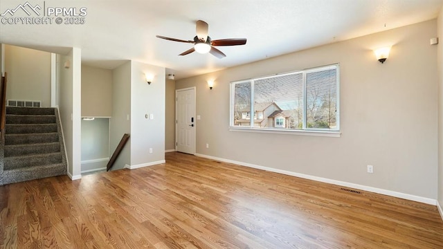 empty room featuring wood finished floors, visible vents, baseboards, ceiling fan, and stairs