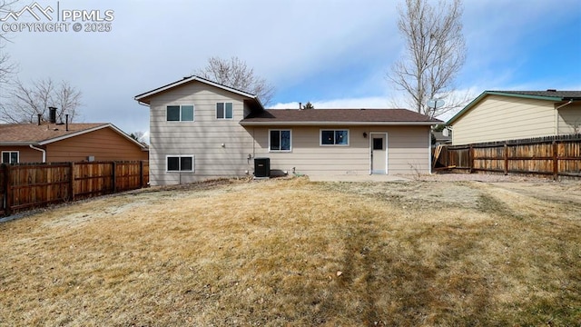 rear view of property featuring a lawn, central AC, and a fenced backyard