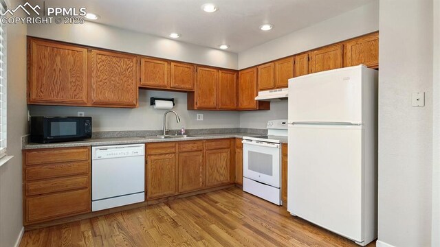 kitchen with white appliances, a sink, light wood-style floors, under cabinet range hood, and brown cabinets