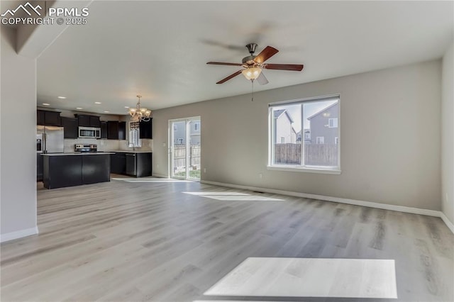 unfurnished living room featuring baseboards, ceiling fan with notable chandelier, and light wood finished floors