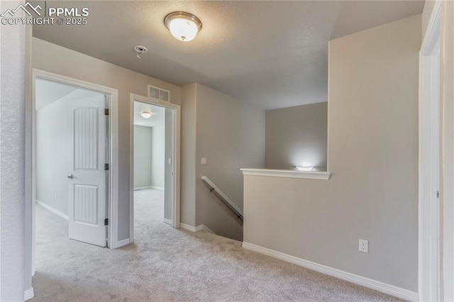 hall with an upstairs landing, visible vents, baseboards, and carpet