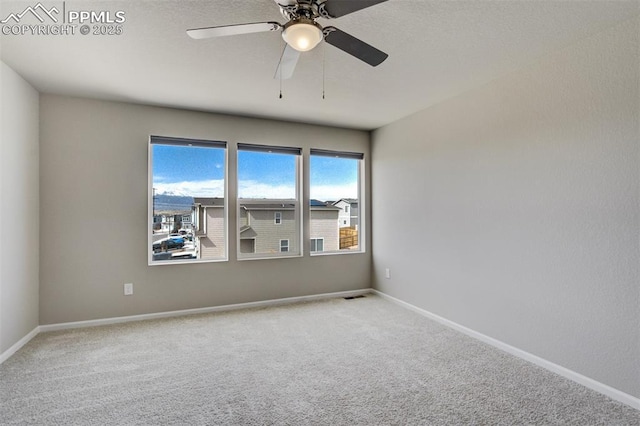 carpeted spare room with visible vents, baseboards, and ceiling fan