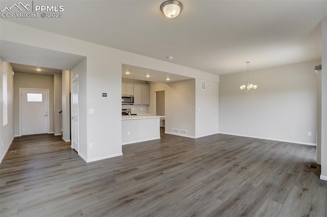 unfurnished living room with a chandelier, baseboards, and wood finished floors