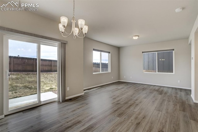 unfurnished room with a notable chandelier, wood finished floors, and baseboards