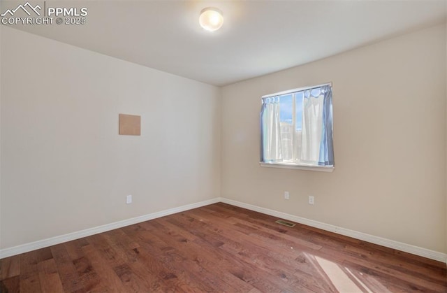 spare room featuring wood finished floors, visible vents, and baseboards