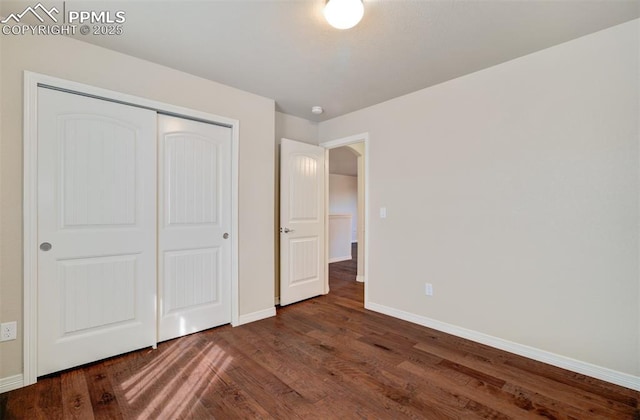 unfurnished bedroom with dark wood-style floors, a closet, and baseboards