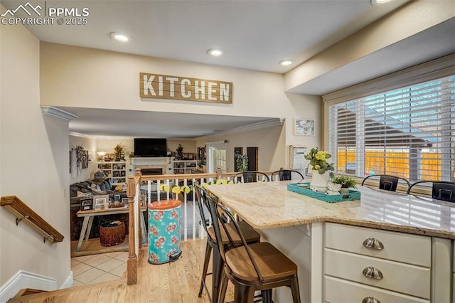 kitchen with a fireplace, light wood-style flooring, ornamental molding, light stone countertops, and a kitchen breakfast bar