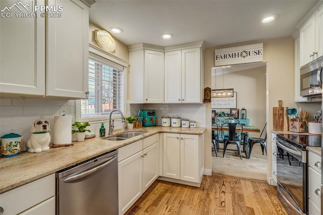 kitchen featuring stainless steel appliances, a sink, white cabinets, light wood-type flooring, and decorative backsplash