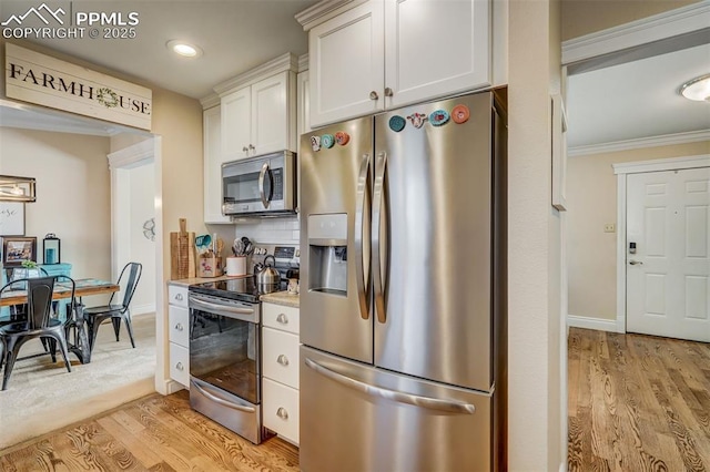 kitchen featuring white cabinets, light countertops, ornamental molding, appliances with stainless steel finishes, and light wood-type flooring