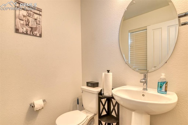 bathroom with a textured wall, a sink, and toilet