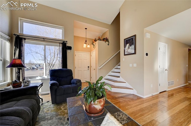 living area with a high ceiling, wood finished floors, visible vents, baseboards, and stairs