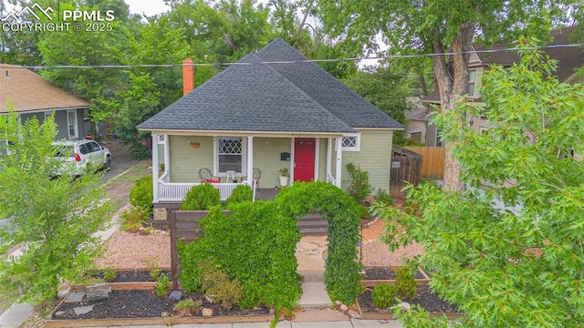 bungalow featuring a porch, fence, roof with shingles, and a chimney