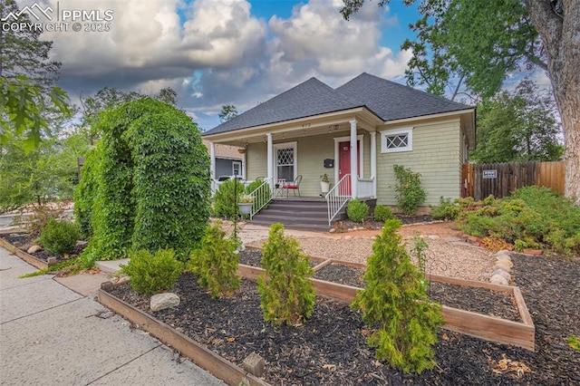 bungalow featuring covered porch, a vegetable garden, roof with shingles, and fence