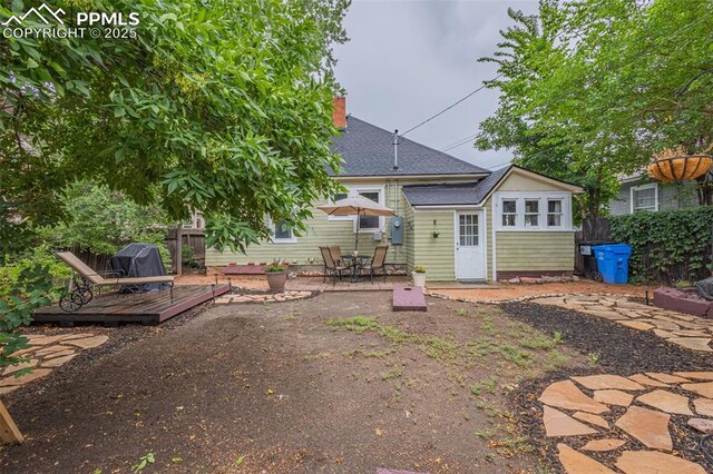 back of house with fence, roof with shingles, a wooden deck, a chimney, and a patio area