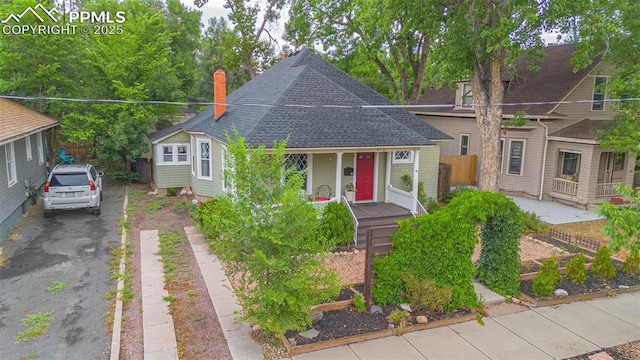 view of front of home with fence, driveway, roof with shingles, covered porch, and a chimney
