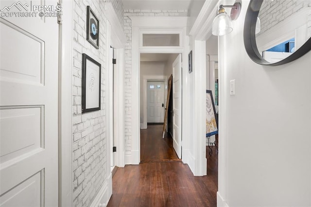 hallway featuring baseboards, dark wood-type flooring, and brick wall