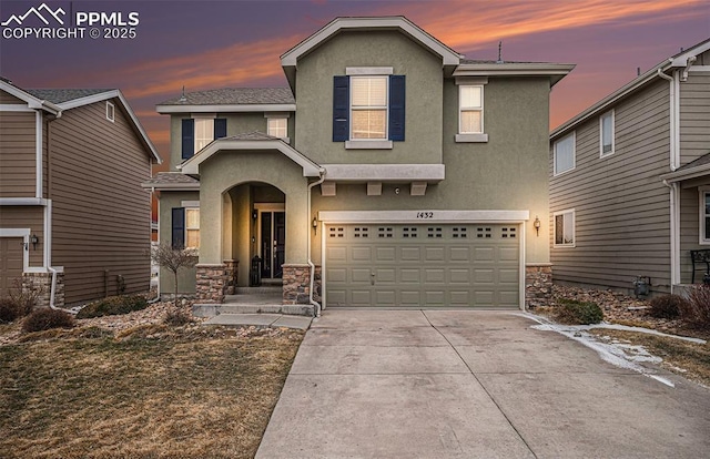 traditional home featuring a garage, stone siding, driveway, and stucco siding