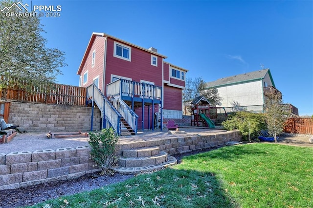 back of house with a deck, a playground, fence, stairway, and a lawn