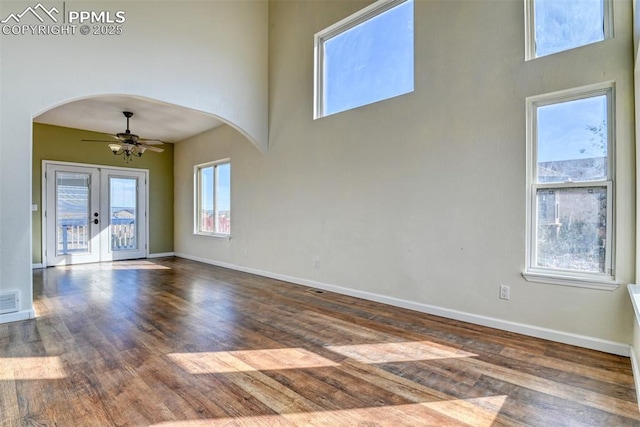 empty room featuring a ceiling fan, arched walkways, baseboards, and wood finished floors