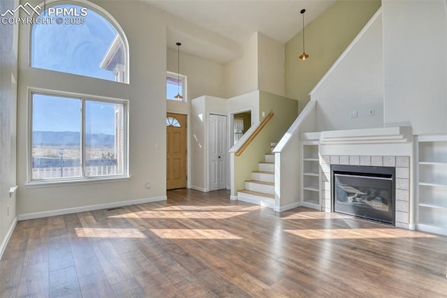 unfurnished living room with baseboards, a tile fireplace, stairway, wood finished floors, and a high ceiling