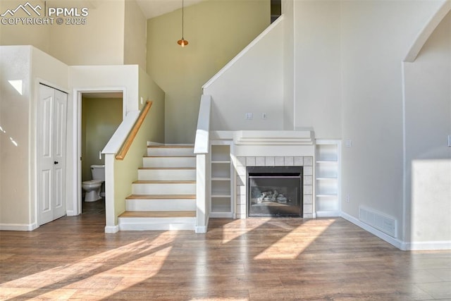 interior space with wood finished floors, a towering ceiling, visible vents, baseboards, and a tiled fireplace