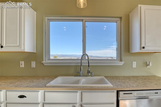 kitchen featuring white cabinets, light countertops, dishwasher, and a sink