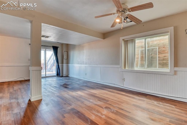 empty room with a wainscoted wall, ceiling fan, visible vents, and wood finished floors