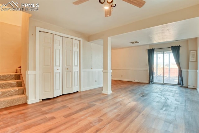 interior space with a wainscoted wall, visible vents, light wood-style flooring, a ceiling fan, and stairs