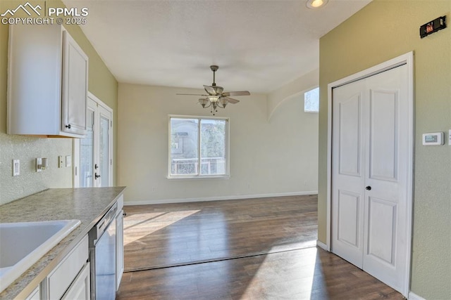 kitchen with a sink, stainless steel dishwasher, dark wood finished floors, and baseboards