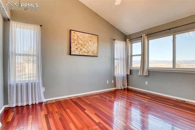 empty room featuring lofted ceiling, hardwood / wood-style floors, visible vents, and baseboards