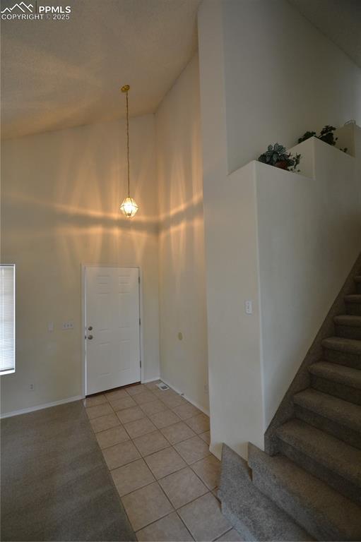 foyer entrance featuring light tile patterned flooring, stairway, and a high ceiling