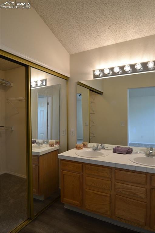 bathroom featuring vaulted ceiling, double vanity, a textured ceiling, and a sink