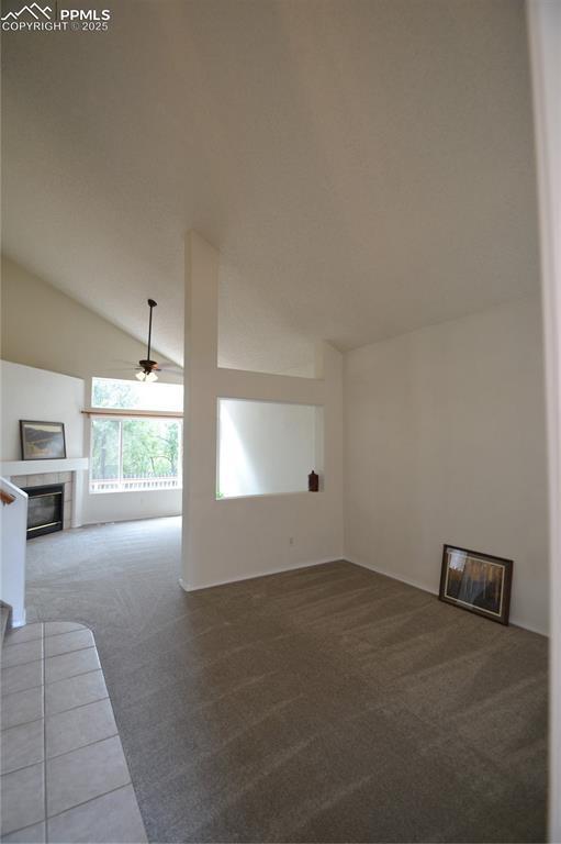 unfurnished living room featuring lofted ceiling, ceiling fan, carpet flooring, and a tile fireplace