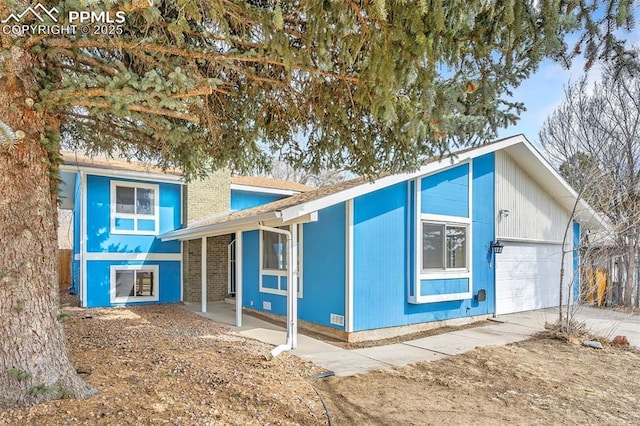 split level home with a garage, brick siding, concrete driveway, and a chimney