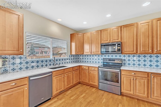 kitchen featuring a sink, light countertops, appliances with stainless steel finishes, light wood finished floors, and tasteful backsplash