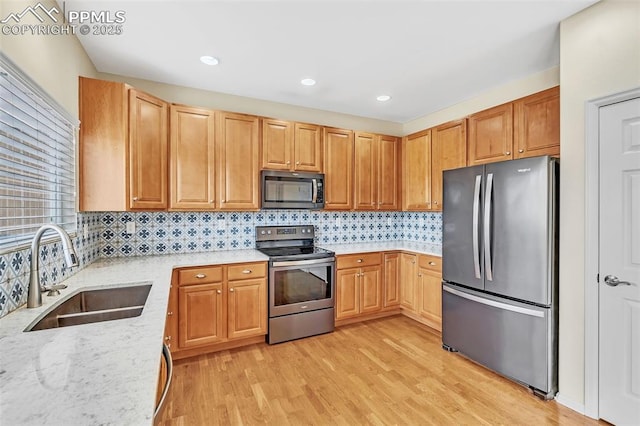 kitchen featuring stainless steel appliances, a sink, light wood-type flooring, backsplash, and light stone countertops