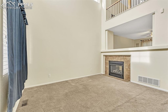 unfurnished living room featuring carpet floors, a towering ceiling, visible vents, and a tile fireplace