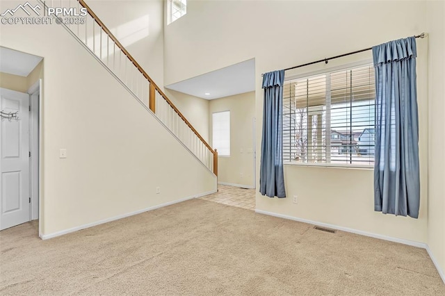 carpeted empty room with stairs, a high ceiling, visible vents, and baseboards