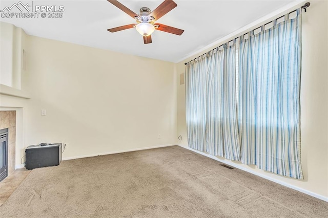 unfurnished living room with baseboards, visible vents, a tiled fireplace, ceiling fan, and carpet