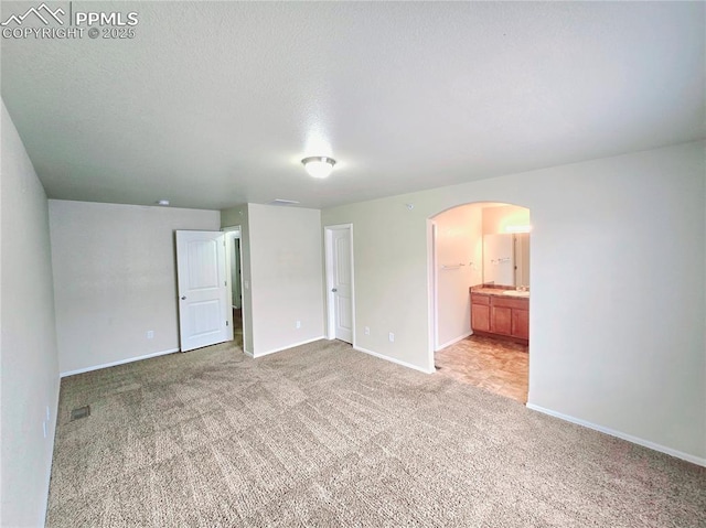 unfurnished bedroom featuring visible vents, baseboards, arched walkways, a textured ceiling, and light carpet