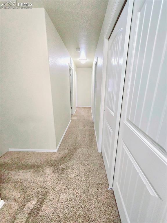 hallway featuring light carpet, a textured ceiling, and baseboards