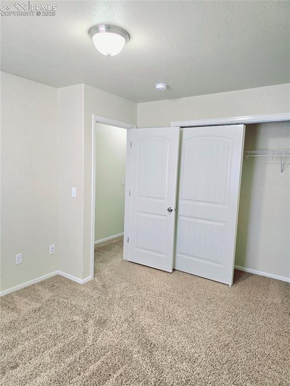 unfurnished bedroom featuring a closet, baseboards, a textured ceiling, and light carpet