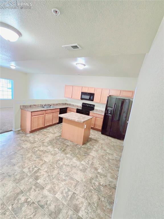 kitchen with visible vents, a kitchen island, light brown cabinetry, light countertops, and black appliances