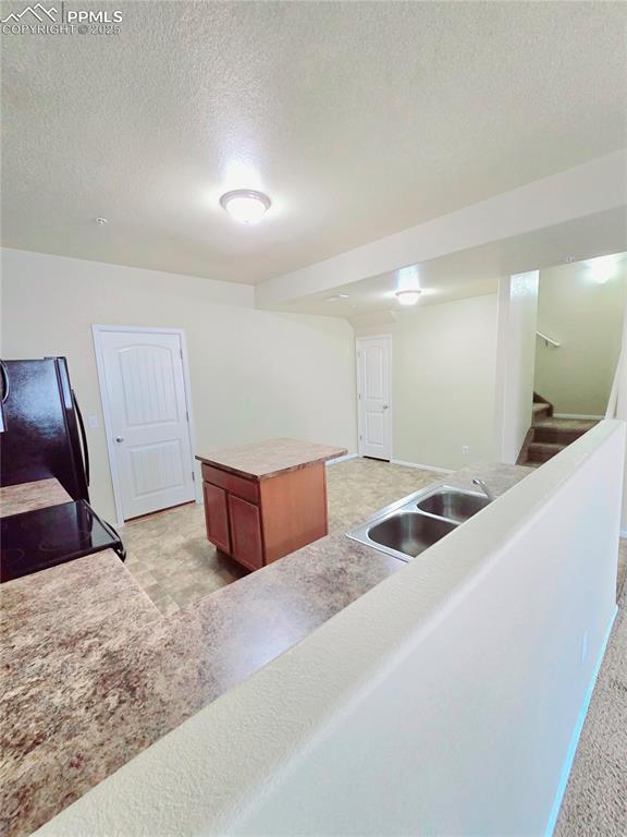 kitchen with a textured ceiling, a kitchen island, freestanding refrigerator, and a sink